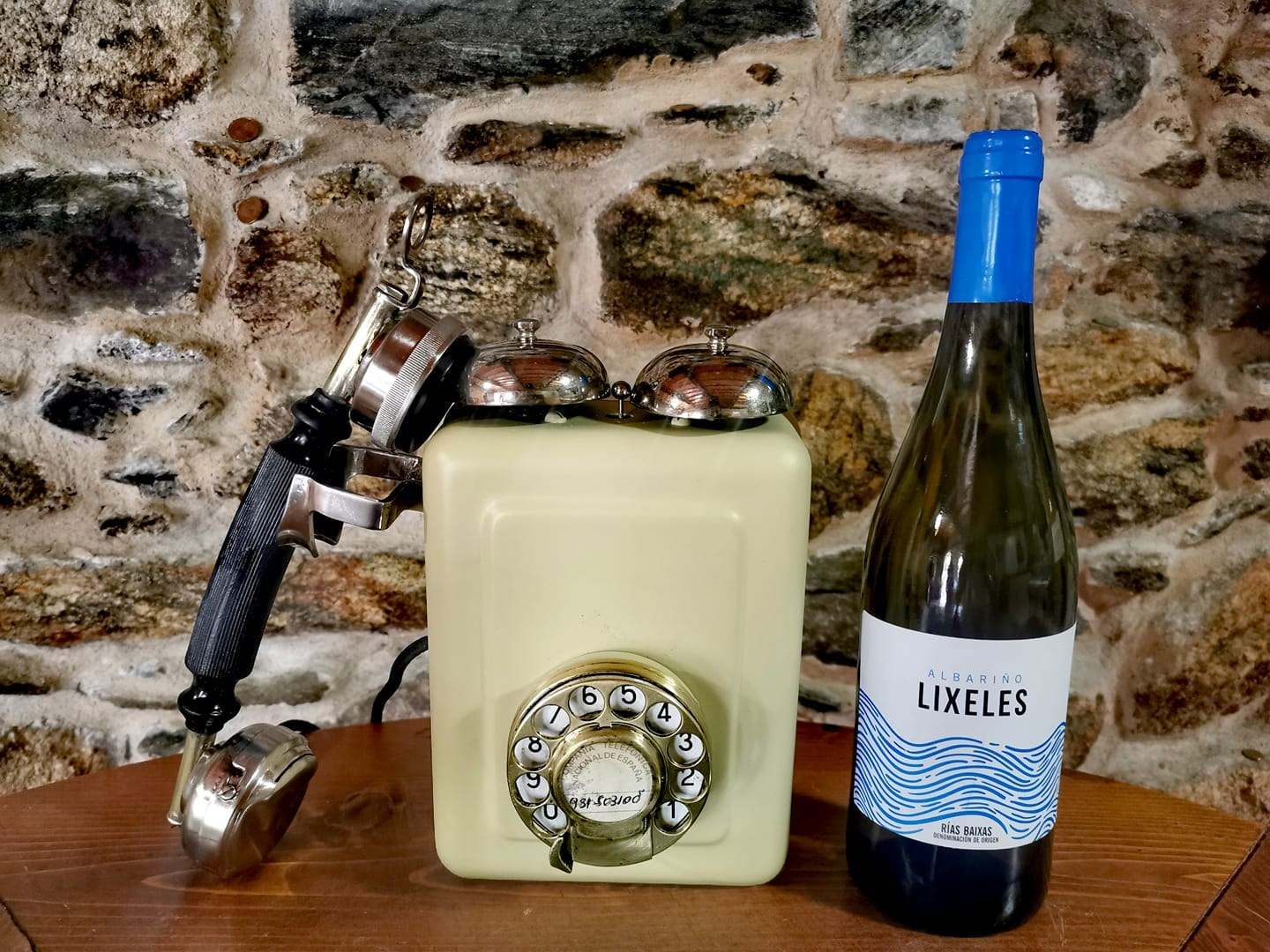 Botella de Lixeles junto a un teléfono antiguo sobre muro de piedra